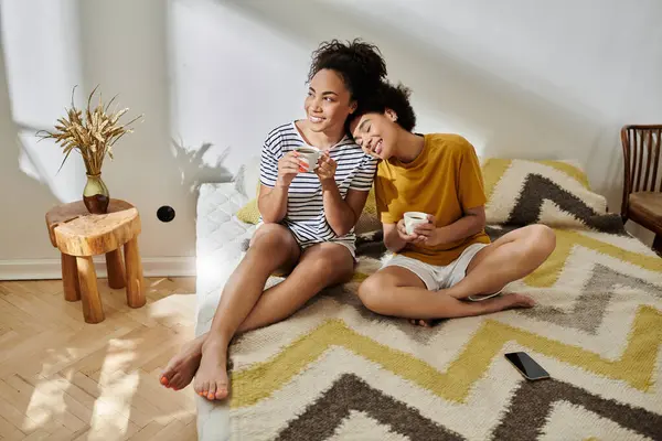 A joyful couple shares laughter while sipping tea on a cozy bed. — Stock Photo