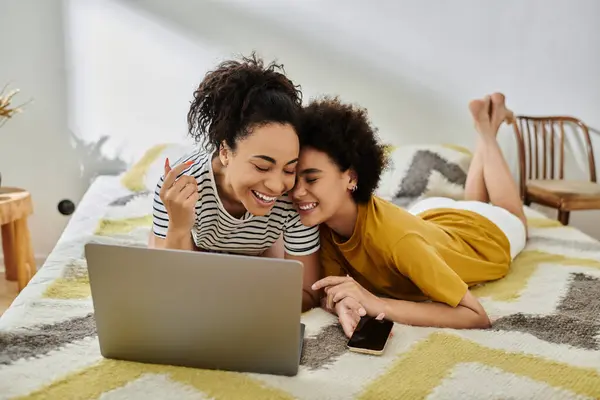 Two women share laughter and closeness while using a laptop in their cozy space. — Stock Photo