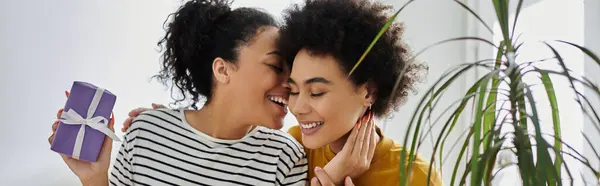 Two women share a loving moment with a gift at home, radiating happiness and connection. — Stock Photo