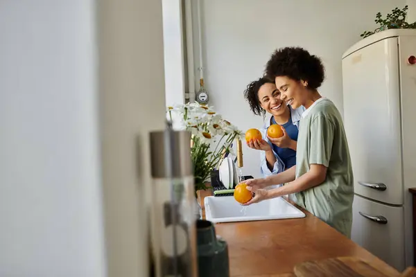 Two women share smiles while washing oranges at their cozy home kitchen. — Stock Photo