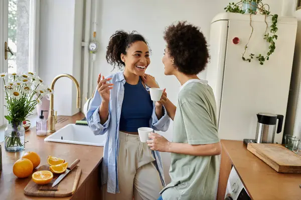 Two women share joyful laughter while sipping tea in their sunny kitchen. — Stock Photo