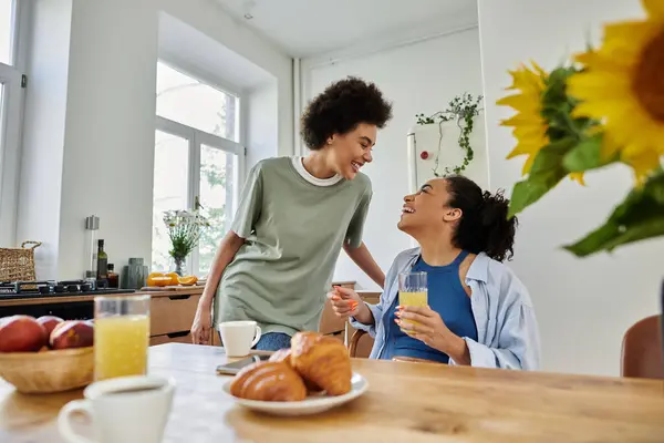 Two women share laughter and drinks while enjoying breakfast together at home. — Stock Photo
