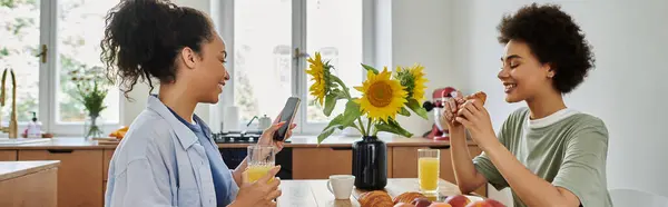 Two women share laughter and breakfast in a sunlit kitchen. — Stock Photo