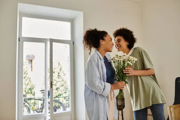 A loving couple shares a joyful moment while holding flowers indoors. — Stock Photo