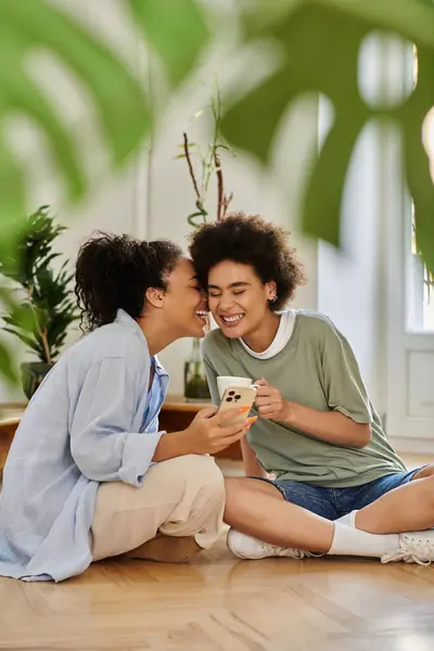 Due donne che condividono risate mentre guardano un telefono nel loro accogliente spazio vitale. — Foto stock