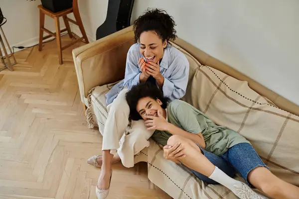 Two women laugh and share a cozy moment together on a comfortable couch. — Stock Photo