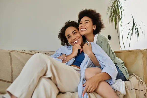 Dos mujeres comparten un abrazo alegre, rodeadas de confort y calidez en casa. - foto de stock