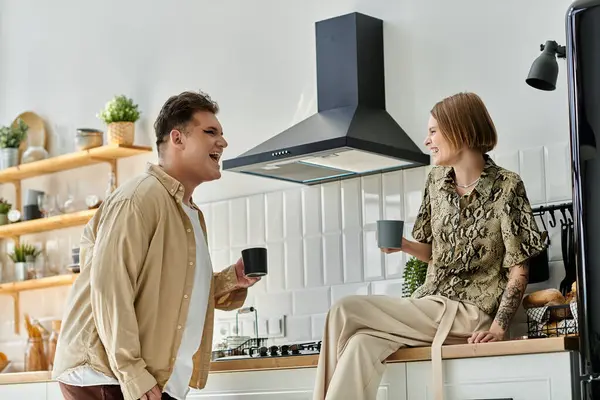 Two friends share laughter and coffee in a warm home kitchen atmosphere. — Stock Photo
