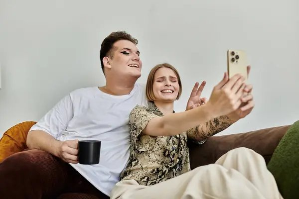 Dos amigos comparten la risa y la alegría mientras capturan una selfie sentida en el sofá. - foto de stock