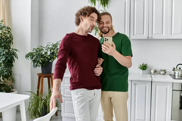 Couple shares a joyful moment while looking at their phone in a bright kitchen. — Stock Photo