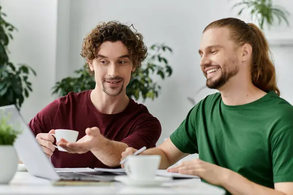 A joyful couple shares coffee and smiles while working at their home table. — Stock Photo