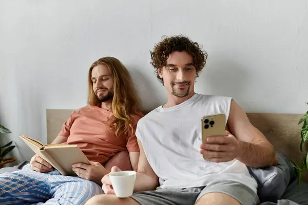 A couple relaxes in bed, sharing a book and phone, surrounded by warmth and love. — Stock Photo