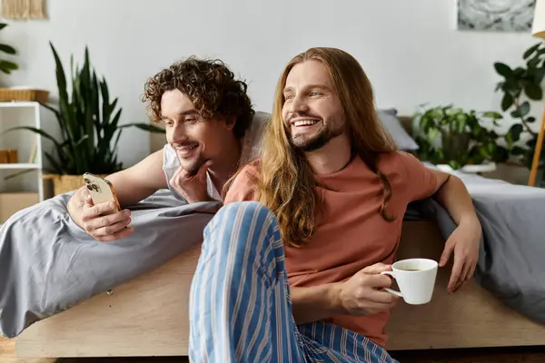 Two men share laughter while enjoying coffee and browsing on a smartphone. — Stock Photo
