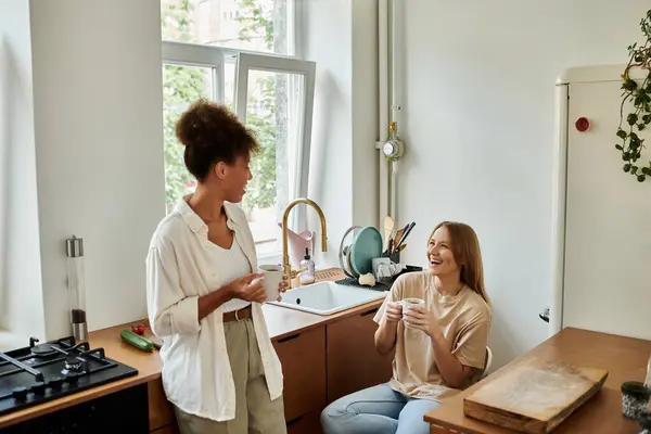 Two partners share laughter and drinks in a bright, inviting kitchen. — Stock Photo