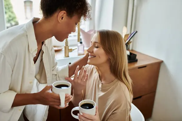 Two partners share a tender moment while holding steaming mugs of coffee. — Stock Photo