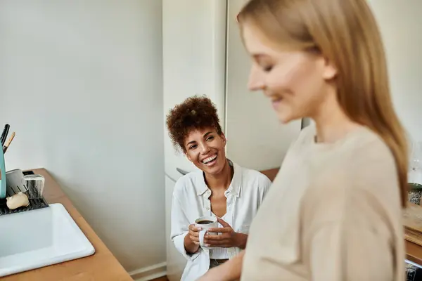Two partners share laughter and warmth while sipping coffee in their kitchen. — Stock Photo