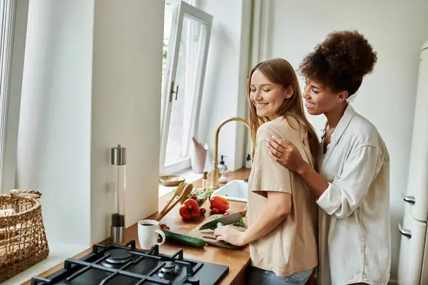 Dos socios preparan alegremente una comida al lado del otro en su acogedora cocina. - foto de stock