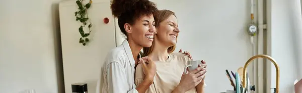 Deux femmes embrassent chaleureusement tout en dégustant des boissons dans une cuisine lumineuse. — Photo de stock