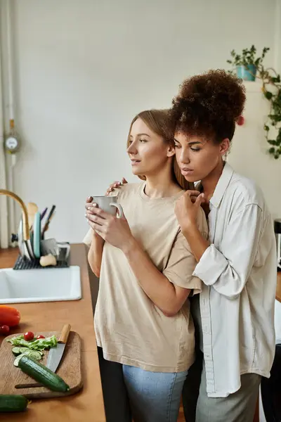 Deux partenaires s'embrassent tout en partageant une boisson chaude dans leur cuisine. — Photo de stock