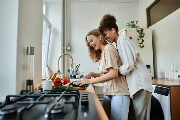 Couple prépare joyeusement un repas tout en embrassant dans une cuisine ensoleillée. — Photo de stock