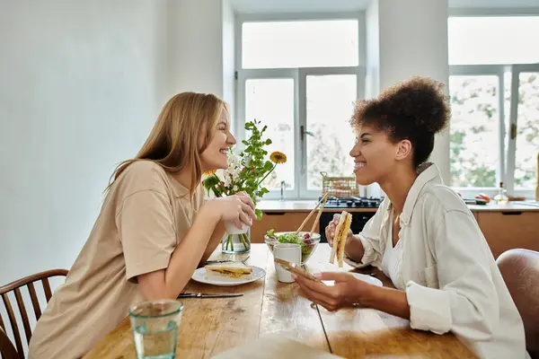 Una coppia felice condivide una risata e un pasto a un tavolo da cucina illuminato dal sole. — Foto stock