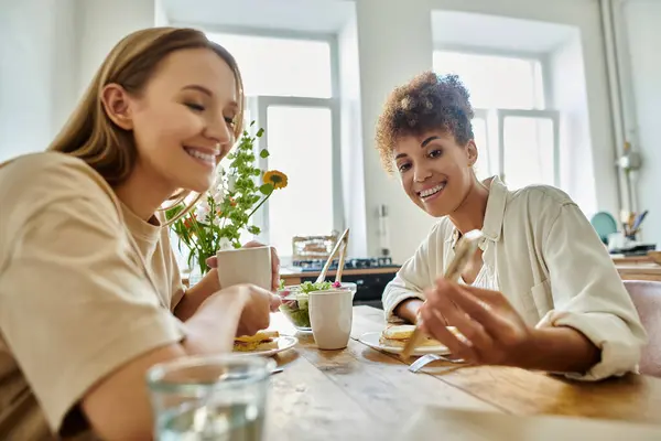 Two partners share laughter and delicious food in a sunlit kitchen. — Stock Photo
