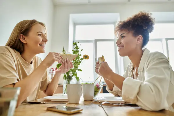Una coppia felice condivide risate e cibo a un tavolo illuminato dal sole pieno di piatti freschi. — Foto stock
