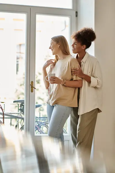 Two partners share a cozy moment, smiling and standing side by side by the window. — Stock Photo