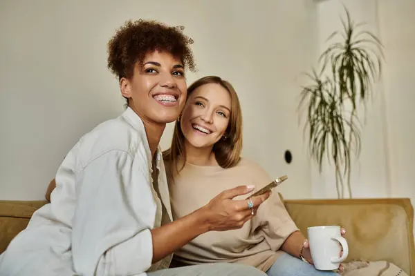 A happy couple relaxes on a couch, sharing laughter and a warm drink. — Stock Photo