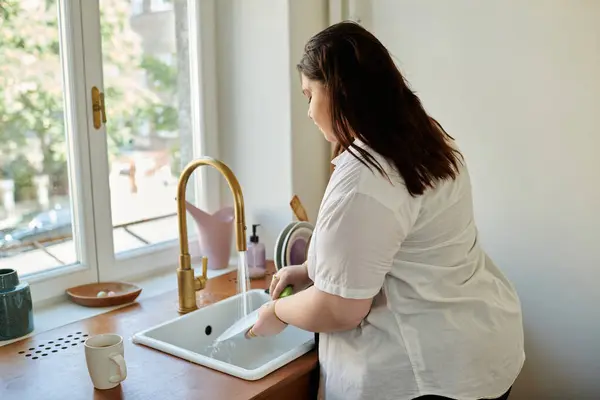 Eine Frau lächelt beim Geschirrspülen in ihrer sonnigen Küche. — Stockfoto