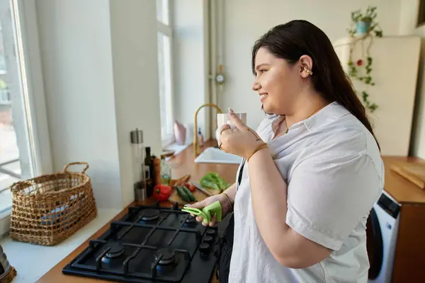 Uma mulher plus size sorri enquanto toma chá e prepara ingredientes em casa. — Fotografia de Stock