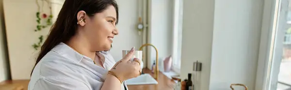 Una mujer alegre bebe té mientras aprecia la vista desde su cocina. - foto de stock