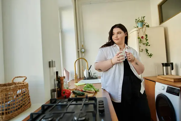 A confident woman enjoys her morning coffee while standing in a bright kitchen. — Stock Photo