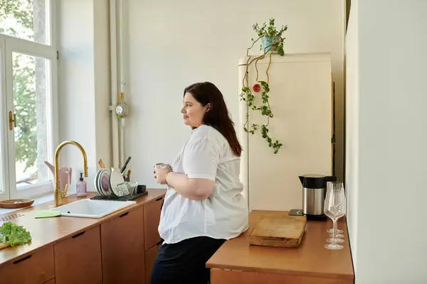 A woman relaxes in her kitchen, sipping a warm beverage and enjoying the sunlight. — Stock Photo