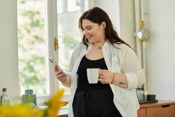 A plus size woman relaxes at home, sipping coffee while texting happily. — Stock Photo