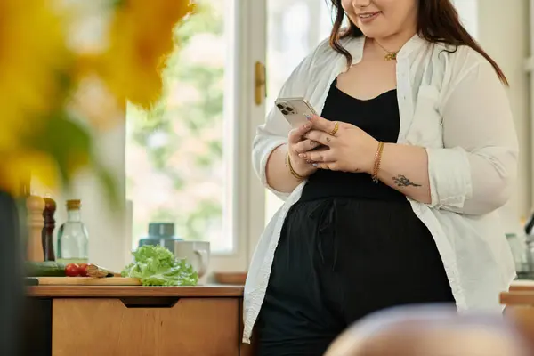 A beautiful woman checks her phone while preparing a meal in her kitchen. — Stock Photo
