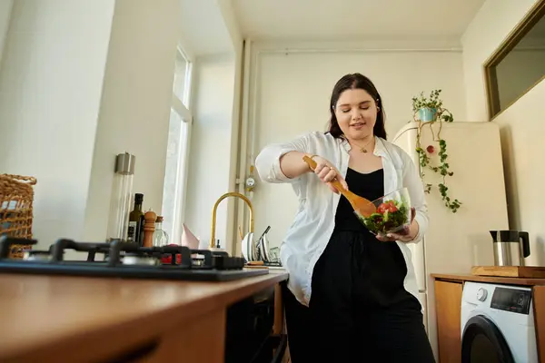 A beautiful woman joyfully mixes fresh ingredients in her kitchen. — Stock Photo