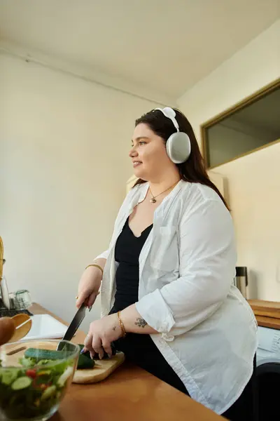 A joyful woman prepares a fresh meal while listening to music at home. — Stock Photo