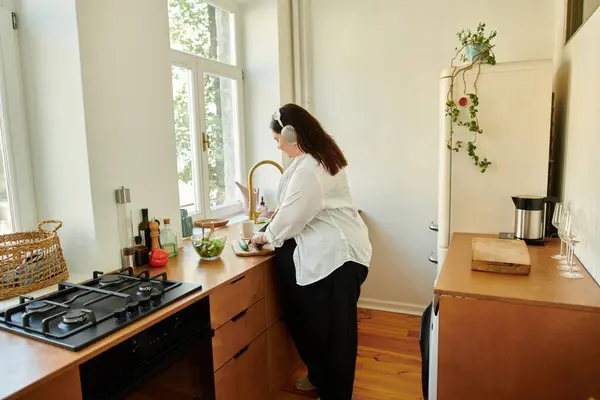 A joyful plus size woman prepares fresh ingredients in her bright kitchen. — Stock Photo