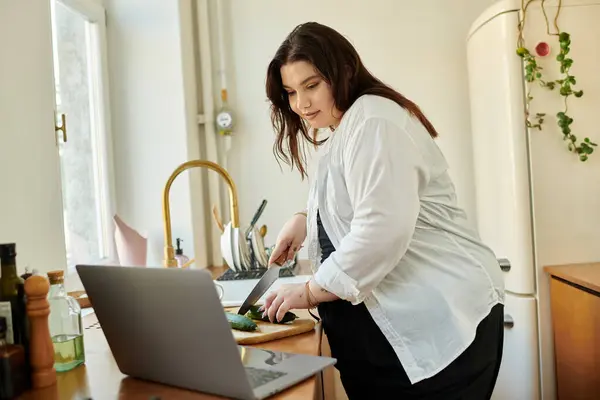 A plus size woman joyfully prepares a meal while following a recipe online. — Stock Photo
