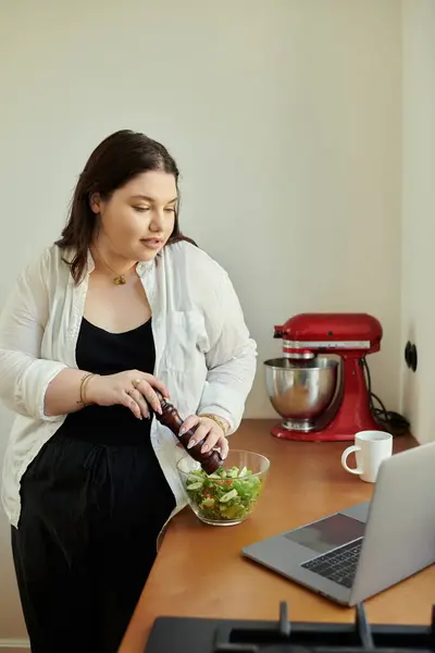 Une femme assaisonne amoureusement une salade tout en se tenant à son comptoir de cuisine. — Photo de stock