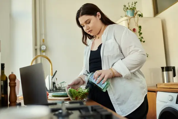Uma mulher derrama vestir-se sobre uma salada fresca e fazer em sua cozinha brilhante. — Fotografia de Stock