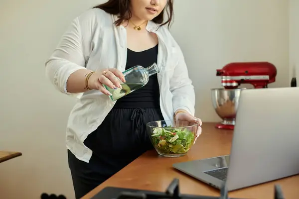 Una donna allegra mescola un'insalata colorata con un pizzico di olio d'oliva a casa.. — Foto stock