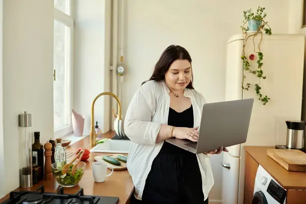 A plus size woman engages with her laptop while enjoying her kitchen. — Stock Photo