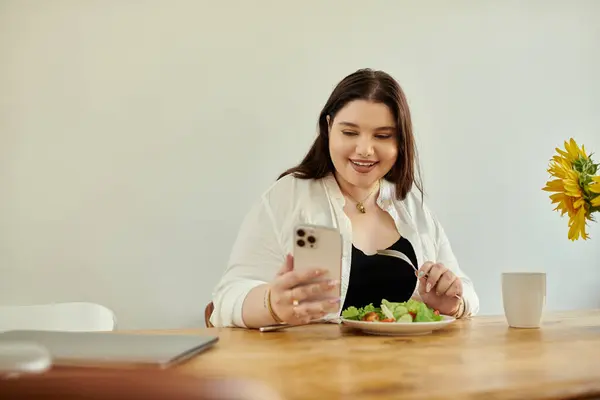 A joyful woman savors her delicious meal while connecting with her phone. — Stock Photo