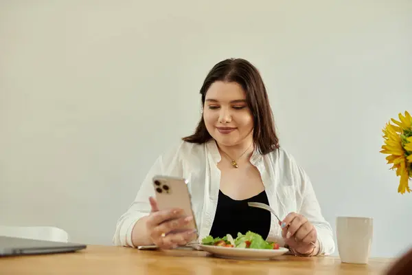 Una bella donna plus size gode il pranzo guardando il suo telefono. — Foto stock