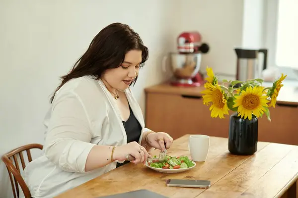 Eine schöne Frau genießt einen köstlichen Salat, während sie an ihrem Esstisch sitzt. — Stockfoto