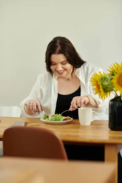 Eine fröhliche Frau genießt einen nahrhaften Salat am Küchentisch. — Stockfoto
