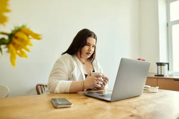 A plus size woman savors coffee while focused on her laptop at home. — Stock Photo
