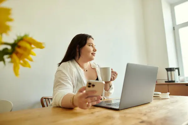 A plus size woman relaxes with coffee and her smartphone in a sunlit room. — Stock Photo
